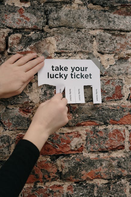 A pair of hands with light skin and black sleeves are attaching a torn paper sign to an aged brick wall. The sign reads 'take your lucky ticket' and has several tear-offs labelled 'lucky ticket,' with some partially ripped off. In the background, the brick wall displays a weathered surface with varying shades of red, orange, and gray, showing the rough texture typical of older masonry. This scene captures a close-up of the hands and the sign, emphasizing the act of posting the message against the rustic brick backdrop. The setting appears to be outdoors or in a space with exposed brickwork, relevant to the context of moving or relocation logistics, although the image does not show moving equipment or furniture.